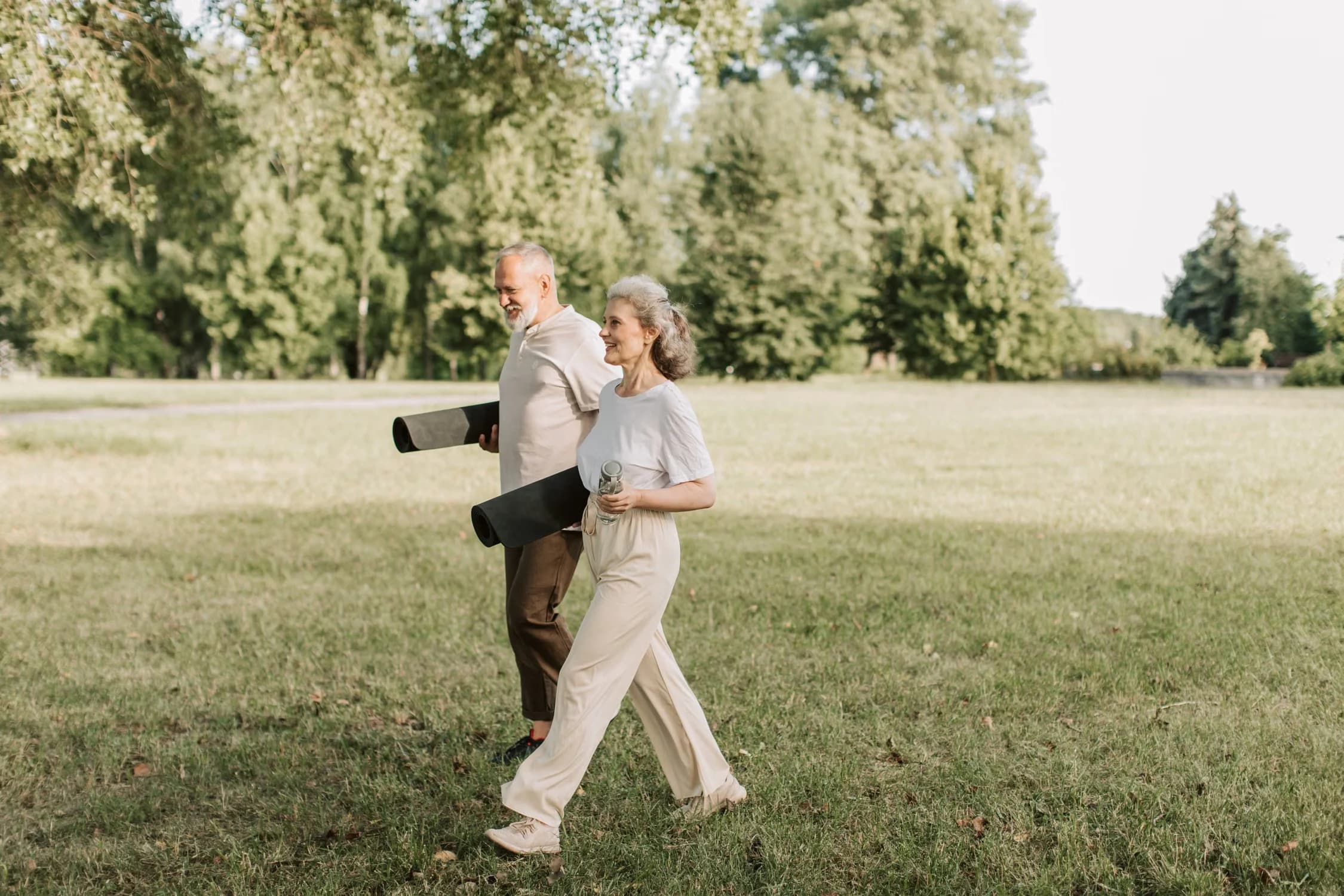 Older adults walking through a park carrying exercise mats