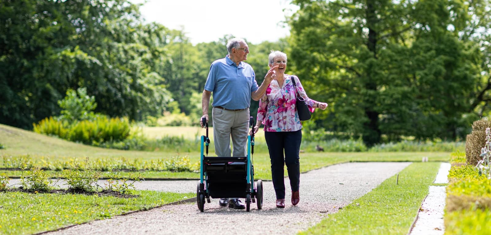 An older couple walking in a park with a walking aid