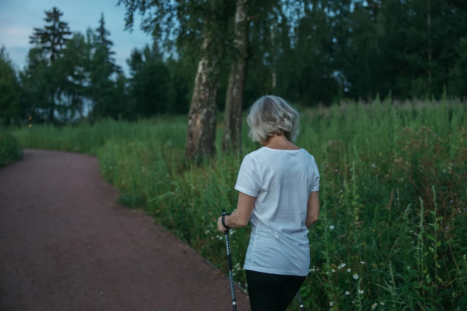 A woman walking along a park trail with walking poles