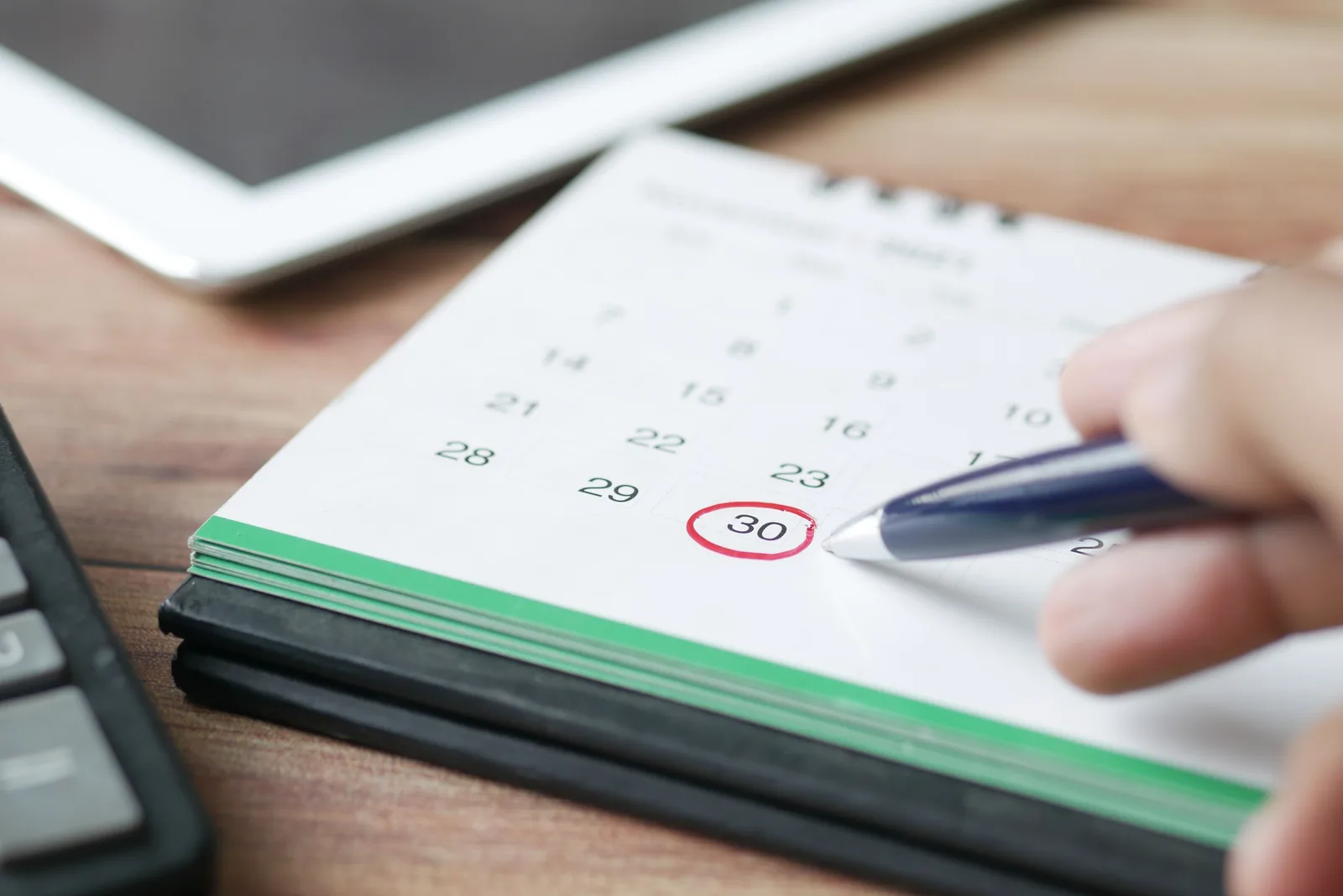 A hand circling a follow-up date on a desk calendar