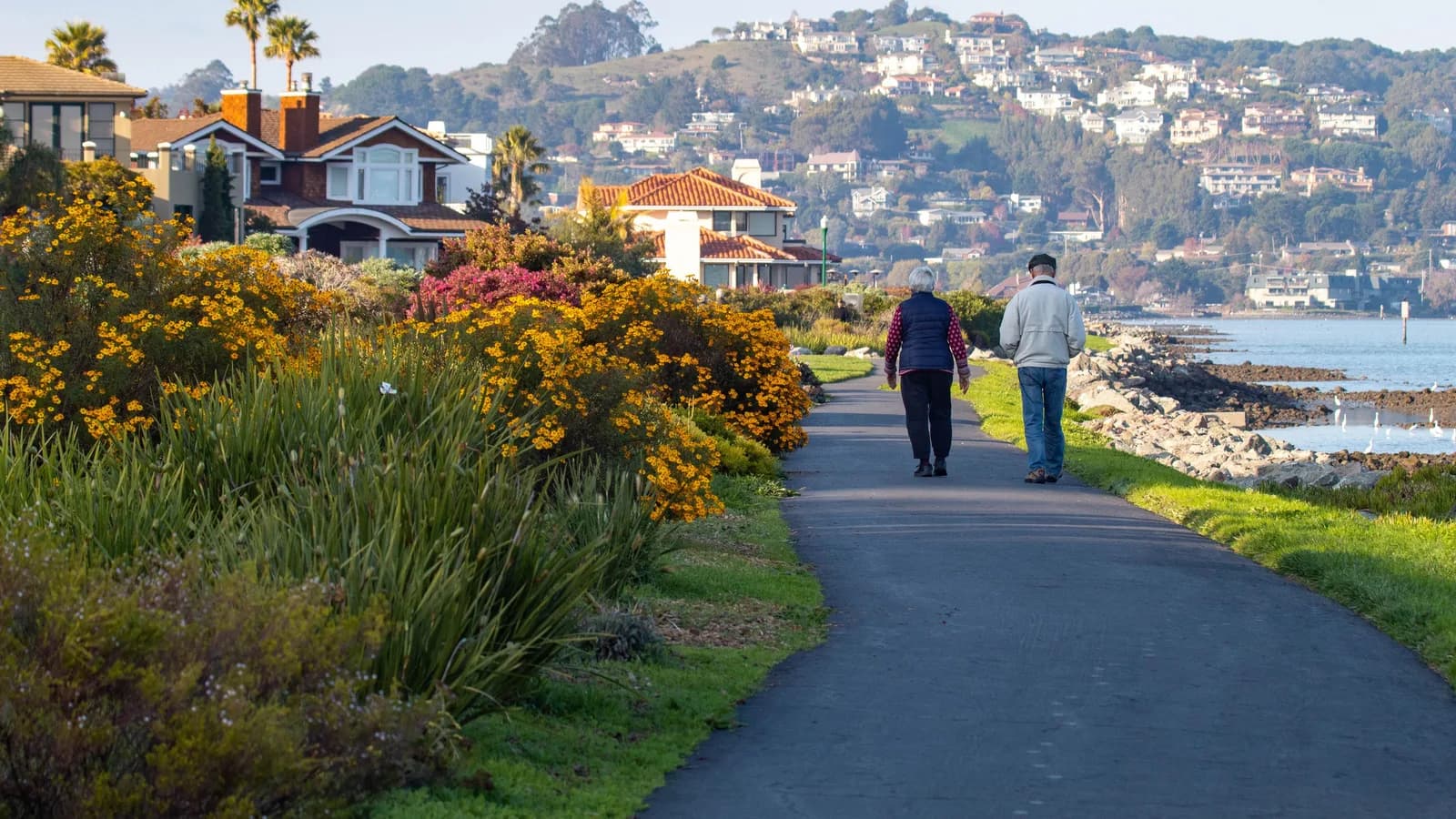 An older couple walking along a coastal waterfront path