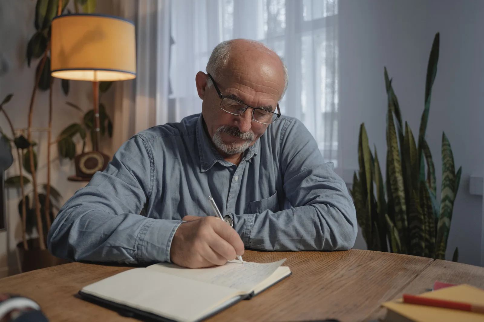 An older man writing notes in a notebook at home